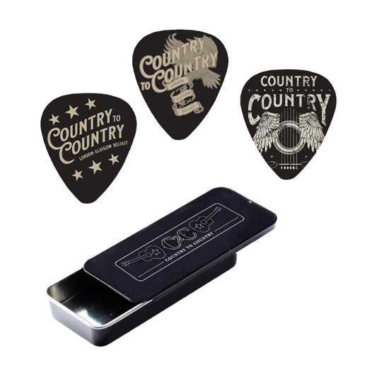 The Plectrum Set from C2C Country To Country Store features three black guitar picks, each with unique Country to Country graphics, displayed above a matching black metal case with sliding lid and logo.