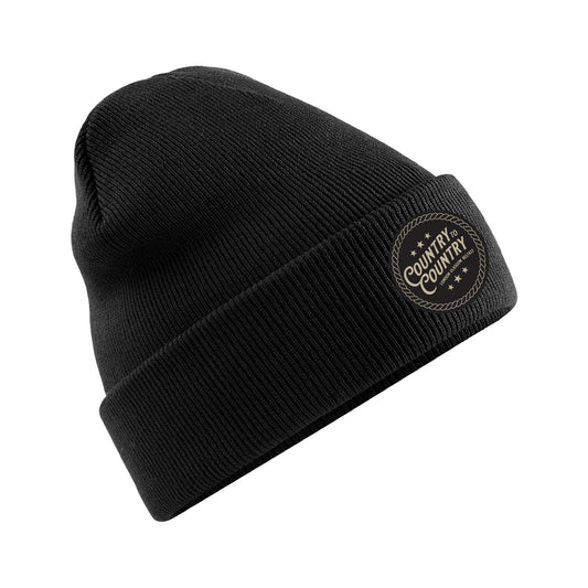 The Black Beanie Hat from C2C Country To Country Store features a folded brim and a circular patch with star accents. Photographed on a white background, this knit hat is perfect for stylish comfort and makes an ideal accessory.