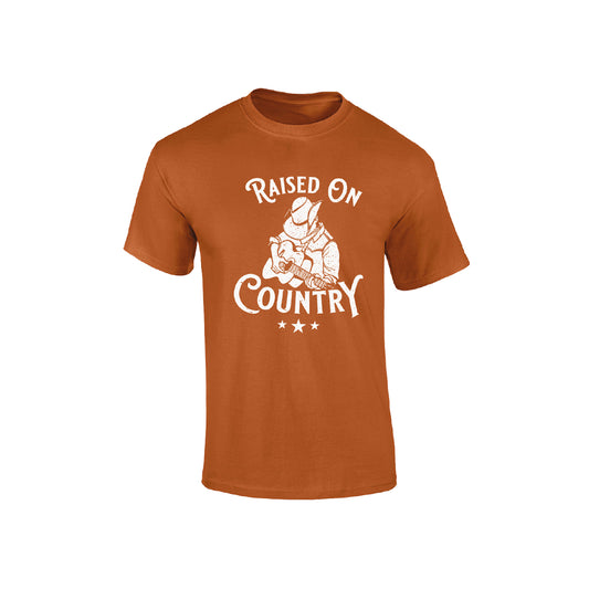 The C2C Country To Country Store Orange Kids T-Shirt features a white graphic of a cowboy hat-wearing guitarist with “Raised on Country” above and below, plus three stars underneath.