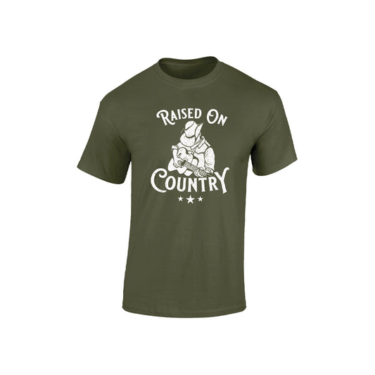 Mill Green Kids T-Shirt by C2C Country To Country Store features an olive green color with a white graphic of a cowboy kneeling and tipping his hat above the words Raised On Country and three stars underneath.