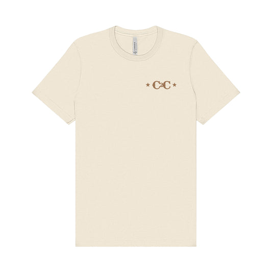 The Western Cowboy Natural T Shirt by C2C Country To Country is a beige unisex tee with a small brown CC logo and two stars on each side, printed on the left chest using eco-friendly DTG printing.
